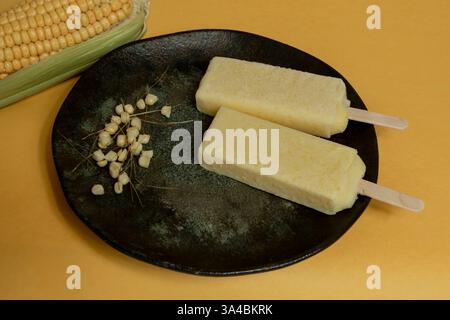 Popsicles de maïs jaunes fondant dans la plaque avec des grains de maïs sur un fond orange. Banque D'Images