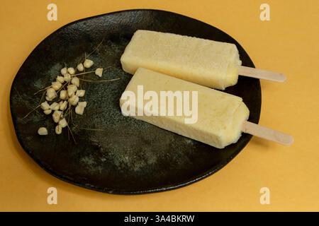 Popsicles de maïs jaunes fondant dans la plaque avec des grains de maïs sur un fond orange. Banque D'Images