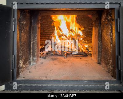 Un four à bois avec un feu lumineux et crépitant et des bûches brûlantes à l'intérieur, se réchauffant pour la cuisson de pizza. Banque D'Images