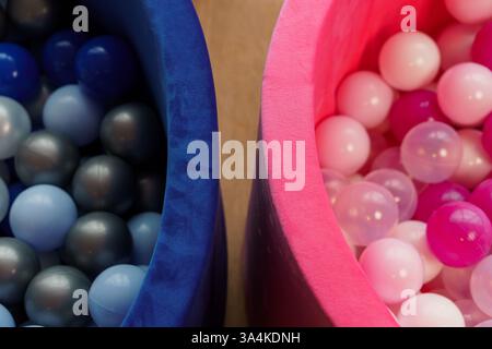 Vue rapprochée de récipients bleus et roses remplis de boules de fosse à boules en plastique colorées créant une composition abstraite symétrique. Banque D'Images