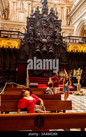 Une femme portant une robe rouge frappante et des lunettes de soleil regarde le plafond d'une belle église de Cordoue en Espagne tandis qu'un jeune couple à l'arrière-plan semble avoir une dispute domestique. Banque D'Images