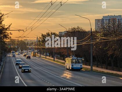 Une rue de ville éclairée par des lumières chaudes du soir, avec la circulation en mouvement régulier. Les phares et les feux arrière créent une lueur dynamique, qui se reflète sur nous Banque D'Images