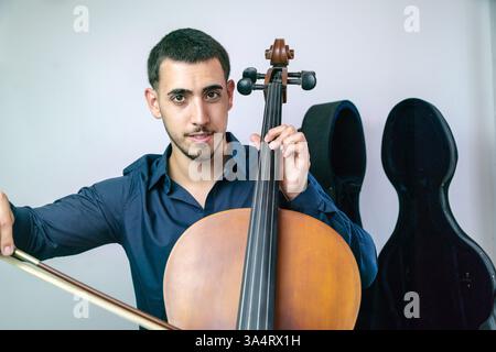 Jeune musicien jouant du violoncelle avec arc et cordes sur fond blanc.. Banque D'Images