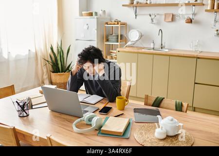 Un jeune homme asiatique étudie attentivement dans sa cuisine, entouré de livres et de matériaux. Banque D'Images