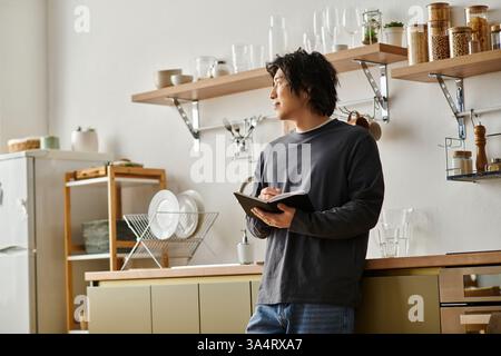 Un jeune homme concentré étudie en ligne à la maison tout en prenant des notes dans son cahier. Banque D'Images