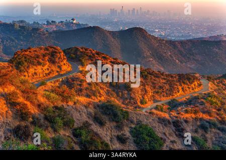 Des sentiers de randonnée sinueux sillonnent Griffith Park, menant à l'observatoire Griffith, avec des vues brumeuses sur le centre-ville de Los Angeles en arrière-plan au coucher du soleil Banque D'Images