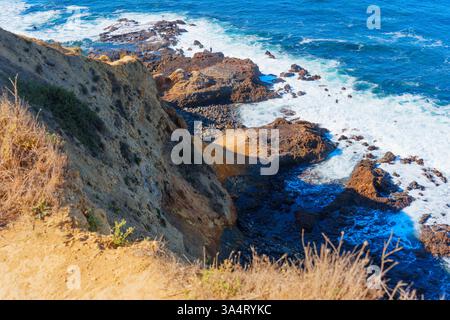 Seul pêcheur se tient sur un terrain rocheux à Bluff Cove, jetant une ligne dans l'océan Pacifique bleu vibrant sous la lumière du soleil, mettant en valeur le sauvage Banque D'Images