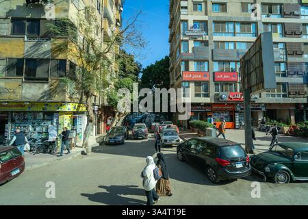 Le Caire, Égypte - 13 janvier 2025 : une vue de rue animée au Caire capturée depuis un bus touristique, montrant des piétons, des voitures garées et des bâtiments avec var Banque D'Images