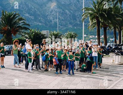 Monténégro, Kotor - 13 juillet 2024 : grand groupe d'enfants avec des sacs à dos et des adultes debout sur la place près des palmiers Banque D'Images