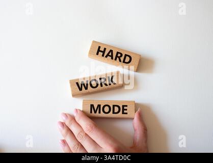 Symbole du mode de travail acharné. Mot concept mode de travail dur sur des blocs de bois. Main d'homme d'affaires. Beau fond blanc. Concept de mode de travail professionnel et dur Banque D'Images