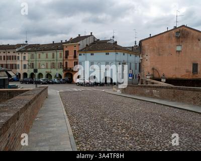 Colorno, Italie 1er mars 2025 Rue pavée menant à la place principale de Colorno, avec des bâtiments colorés avec des arches et la rivière Parme Banque D'Images