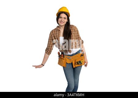 Une ouvrière de construction joyeuse dans une chemise à carreaux et ceinture à outils, penchée légèrement tout en souriant. Isolé sur blanc, parfait pour le travail, constructi Banque D'Images