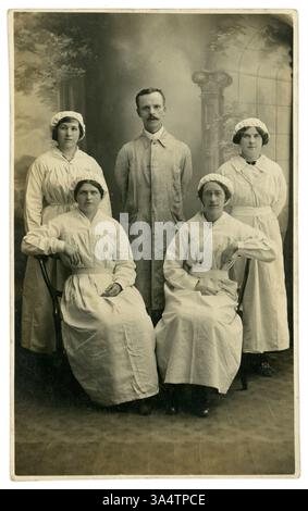 Original WW1 Era studio portrait carte postale des ouvrières de munitions féminines avec contremaître, portant des capuchons élastiques, généralement portés pour garder les cheveux hors de la machinerie. Salopettes en lin blanc, emplacement inconnu, circa 1916, Royaume-Uni Banque D'Images