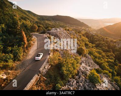 Monténégro, Kotor - 13 juillet 2024 : le cabriolet blanc roule le long d'une route de haute montagne. Drone Banque D'Images