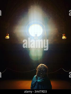 Une femme regarde la lumière du soleil former une croix dans une fenêtre du monastère de Santo Tomás à Ávila, Castilla y Leon, Espagne Banque D'Images