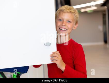 Garçon souriant dans le couloir de l'école ouvrant le casier, l'air excité et joyeux, copiez l'espace Banque D'Images