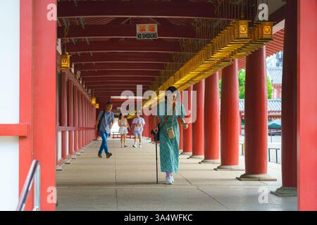 Osaka, Japon - 21 septembre 2024, une vue panoramique d'une galerie avec des colonnes rouges et des lanternes dorées avec des gens marchant, dans le temple bouddhiste Shitenno-ji Banque D'Images
