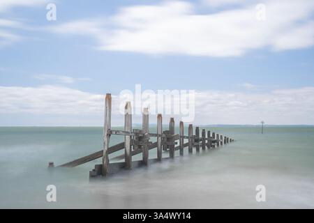 Un vieux groyne sur la plage de West Wittering avec l'île de Wight au loin Banque D'Images