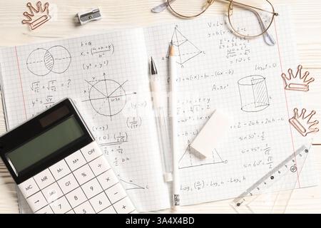 Copybook avec formules mathématiques manuscrites, calculatrice et papeterie sur fond de bois blanc Banque D'Images