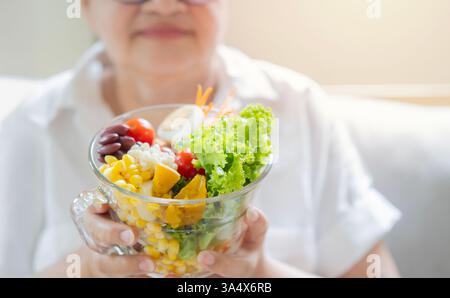 Nutrition du grand âge. Plan recadré d'une femme âgée mangeant une salade de légumes souriante assise sur un canapé à la maison. Mise au point sélective Banque D'Images