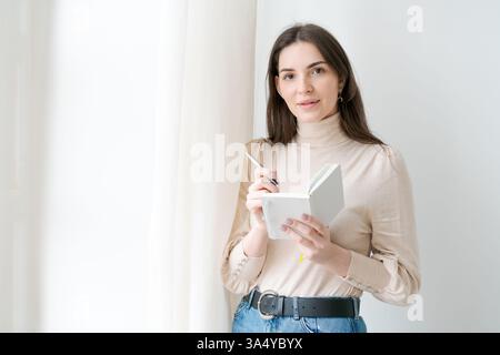 La femme tient un livre et un stylo. Elle sourit. Le livre est ouvert à une page Banque D'Images