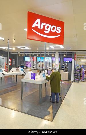 Le modèle de la vue arrière a libéré la femme magasinant sous le grand panneau rouge de la marque du catalogue Argos magasin dans les locaux du supermarché Sainsburys Angleterre Royaume-Uni Banque D'Images