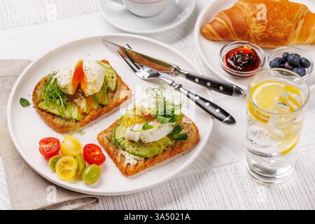 Petit déjeuner avec de délicieux toasts à l'avocat garni d'œufs pochés parfaitement cuits et croissant croustillant avec des baies et de la confiture Banque D'Images