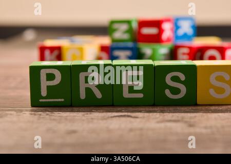 Des blocs colorés sont disposés sur un plancher en bois, affichant en évidence le mot presse parmi diverses autres lettres. Banque D'Images