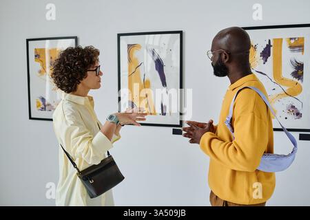 Les jeunes discutent de photographies dans une galerie lors d'une exposition artistique. Un groupe diversifié explorant l'art contemporain, la créativité et l'inspiration à l'intérieur. Parfait pour les visuels de style de vie, de culture et d'éducation. Banque D'Images