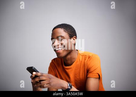 Portrait d'un homme afro-américain cool utilisant un téléphone portable. Cette image de style de vie moderne met en valeur un sujet confiant et souriant sur un fond solide avec un grand espace de copie. Idéal pour les campagnes technologiques, mobiles et sur les réseaux sociaux. Banque D'Images