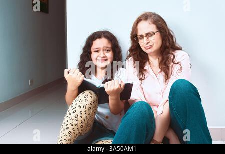 Mère hispanique et fille partagent un moment tranquille de lecture ensemble à la maison. Cette scène tendre convient aux thèmes de la famille, de la parentalité et du style de vie éducatif. Banque D'Images