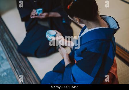 Moments de vie de couple senior dans une maison japonaise traditionnelle. Le cadre calme et culturel évoque le patrimoine et la convivialité intemporelle, adapté à la vie des personnes âgées et aux thèmes familiaux. La composition met l'accent sur la vie privée sans visages, ce qui la rend polyvalente pour les campagnes de style de vie sain. Banque D'Images