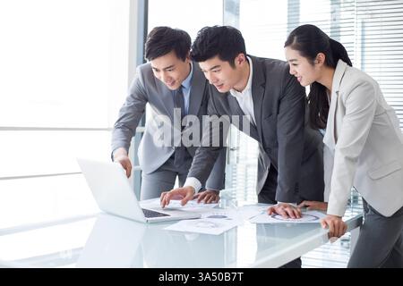 Homme d'affaires chinois avec des collègues travaillant ensemble sur ordinateur portable appuyé sur la table dans le bureau Banque D'Images