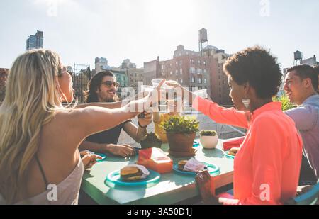 Groupe d'amis divers sur un toit de New York, partageant des rires pendant le coucher du soleil. Une image de style de vie urbain édifiante adaptée aux moments sociaux, à l'amitié et aux campagnes de vie urbaine. Banque D'Images