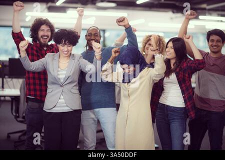 Portrait d'une équipe diversifiée de développeurs de logiciels célébrant le succès dans une startup moderne. Le groupe se tient ensemble, souriant à la caméra, transmettant le travail d'équipe et les réalisations. Parfait pour les thèmes de la technologie, des affaires et de l'entrepreneuriat dans un bureau contemporain. Banque D'Images