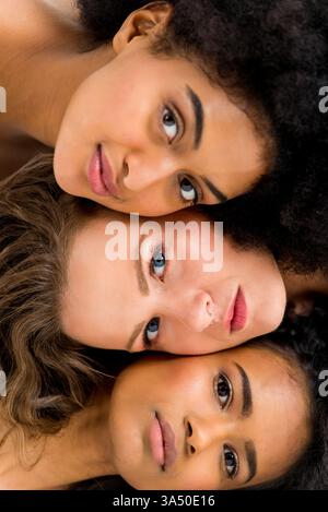 Groupe diversifié de femmes s'appuyant les unes sur les autres à l'intérieur, partageant un moment ludique. Cette composition authentique met en valeur l'amitié, l'inclusion et la connexion féminine pour le style de vie et les articles de magazine. Banque D'Images