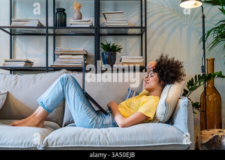 Belle femme latina à la maison avec des cheveux bouclés et un sourire lumineux dans un cadre domestique chaleureux. Ce portrait de style de vie convient au travail à distance, à l'apprentissage en ligne et aux thèmes de la vie quotidienne à la maison. Une image relationnelle pour l'autonomisation des femmes et la vie moderne. Banque D'Images