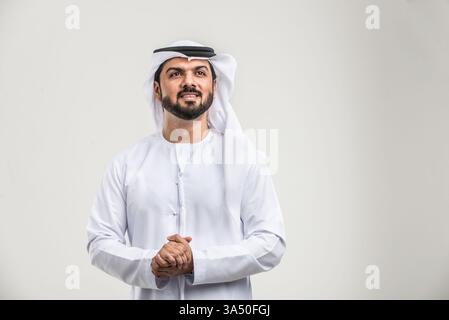 Homme du moyen-Orient regardant loin avec les mains serrées debout contre un fond gris de studio. Portrait composé adapté aux caractéristiques professionnelles, culturelles ou de style de vie. La composition propre et minimale souligne le professionnalisme. Banque D'Images