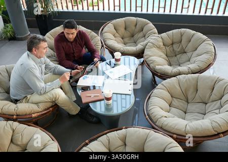Deux professionnels examinent les statistiques sur une tablette lors d’une réunion dans un salon de bureau lumineux. L'image capture le travail d'équipe, l'analyse des données et les discussions stratégiques dans un environnement commercial moderne. Banque D'Images