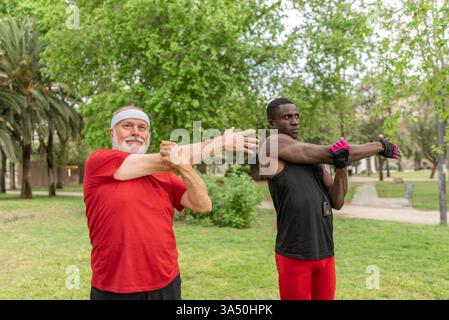 Groupe diversifié d'athlètes masculins dans les vêtements de sport debout et étirent dans un parc ensoleillé. L'image traduit l'entraînement en plein air, le fitness et l'esprit d'équipe, adapté aux campagnes sportives et au contenu de bien-être. Un moment dynamique qui met l'accent sur l'énergie, l'endurance et le bien-être. Banque D'Images