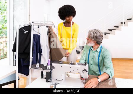 Équipe multiraciale de créateurs de mode collaborant dans un atelier de démarrage de vêtements. Stylistes, designers et couturières travaillent ensemble sur une nouvelle collection. Une image idéale pour le design de mode, le travail d'équipe en studio et les sujets de l'industrie de l'habillement. Banque D'Images