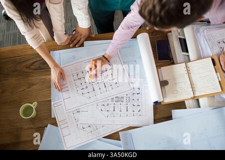 Architectes collaborant dans un bureau, examinant des plans et discutant des plans. L'environnement d'équipe met en valeur le design, le travail d'équipe et la pratique professionnelle. Idéal pour les cabinets d'architecture, la culture de bureau et le marketing de l'industrie du design. Banque D'Images