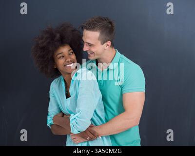 Joyeuse femme noire avec afro et son petit ami blanc partagent un câlin ludique dans un studio à côté d'un tableau noir. Le couple heureux se regarde et sourit, créant un portrait de style de vie chaleureux avec un attrait divers et romantique. Banque D'Images