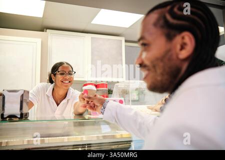 Ouvrière hispanique souriante servant un client masculin dans un magasin de crème glacée Banque D'Images