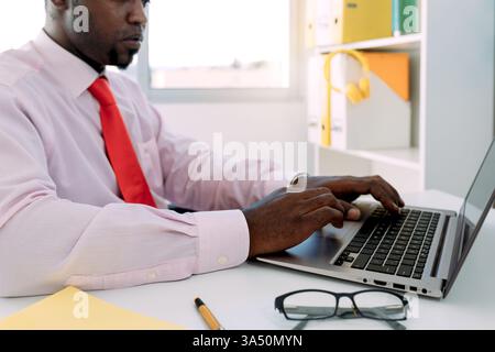Vue latérale d'un entrepreneur noir concentré travaillant sur un netbook dans un bureau moderne. Idéal pour les images conceptuelles professionnelles, entrepreneuriales et professionnelles. Banque D'Images