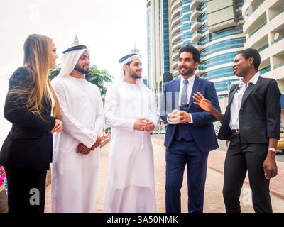 Groupe multiethnique de personnes lors d'une réunion d'affaires aux Émirats arabes Unis, marchant à l'extérieur et parlant d'affaires. La scène extérieure dynamique soutient le travail d'équipe, la diversité et les campagnes de collaboration internationale. Idéal pour les communications d'entreprise et la stratégie de marque. Banque D'Images