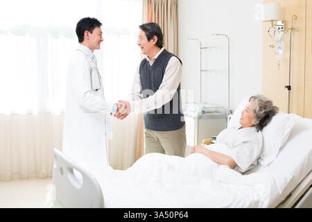 Un couple de aînés chinois respectueux serre la main d'un médecin dans un cadre hospitalier. Cette image exprime la gratitude, les soins et le bien-être dans les contextes de soins de santé. Utile pour les thèmes hospitaliers, de soins aux patients et de services médicaux. Banque D'Images