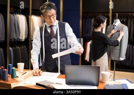 Créateur de mode chinois d'âge moyen et féminin travaillant ensemble sur leur conception dans la boutique de mode Banque D'Images