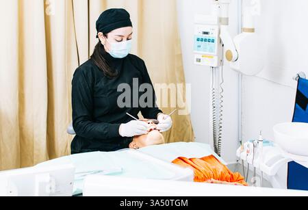 Dentiste nicaraguayenne portant un masque facial et des gants à l'aide d'un miroir d'examen et de broches barbelées dans la guérison des dents d'une patiente senior allongée Banque D'Images