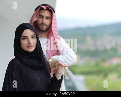 Portrait d'un jeune couple musulman sur un balcon en tenue traditionnelle, posant à l'extérieur. La scène reflète le style culturel, la romance moderne et la vie conjugale dans un contexte moyen-oriental. Banque D'Images